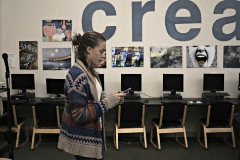 Junior Margo Lusinchi recites her original poetry from her phone at the Open Mic Night in the library. Poetry has served as a creative outlet and therapy for Margo. Photo by Michael Sieffert. 