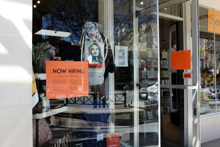 A sign on the window of boutique store Therapy in Mountain View reads Now Hiring. Signs like this have popped up around businesses in the area as low-wage workers move out due to rising housing prices. Mountain View has increased minimum wages at an accelerated pace to combat this issue. Photo by Michael Sieffert.