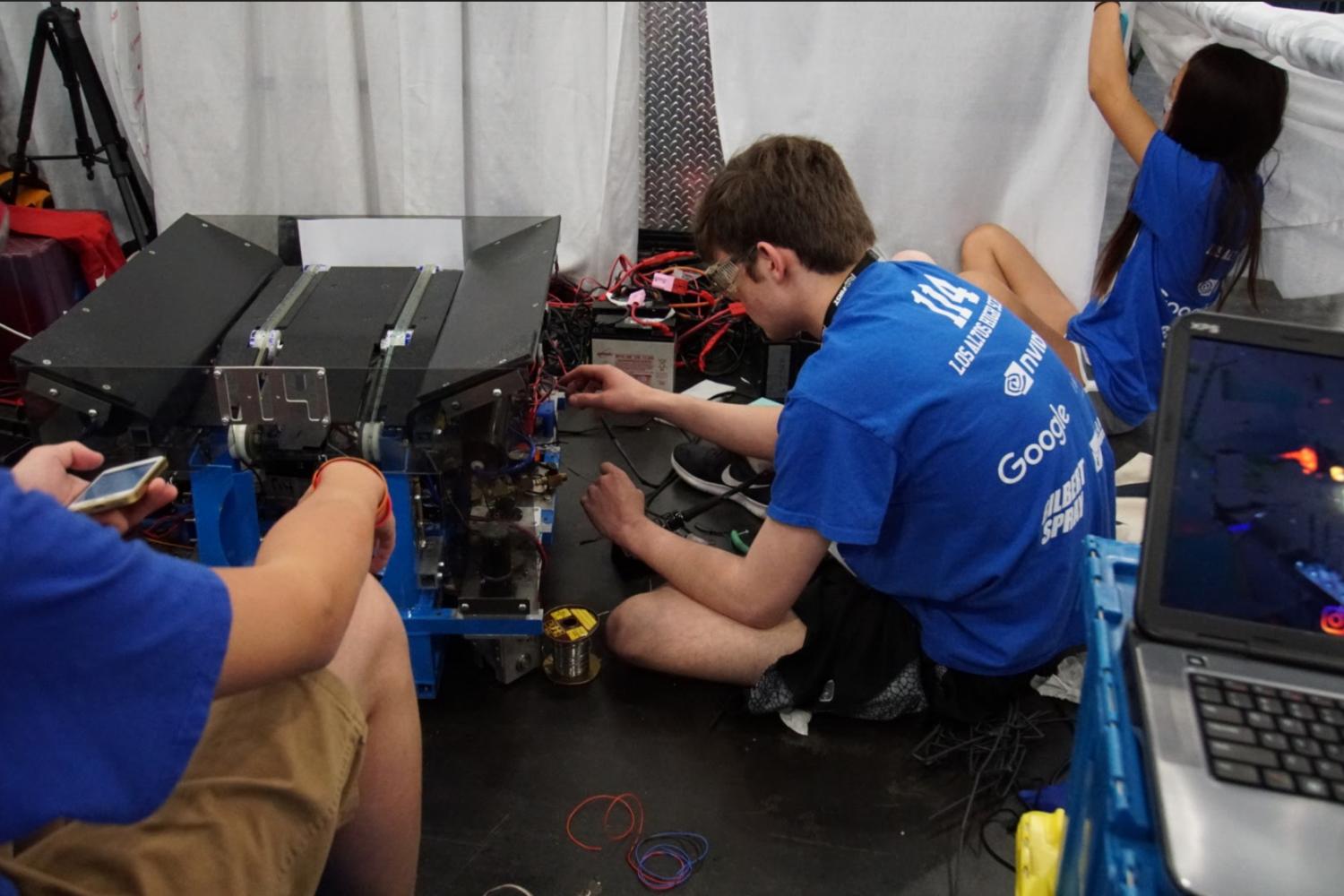 Drive team members Cole Brinsfield (middle) and Michelle Zhu (right) race to fix the wiring on their robot's drivetrain.