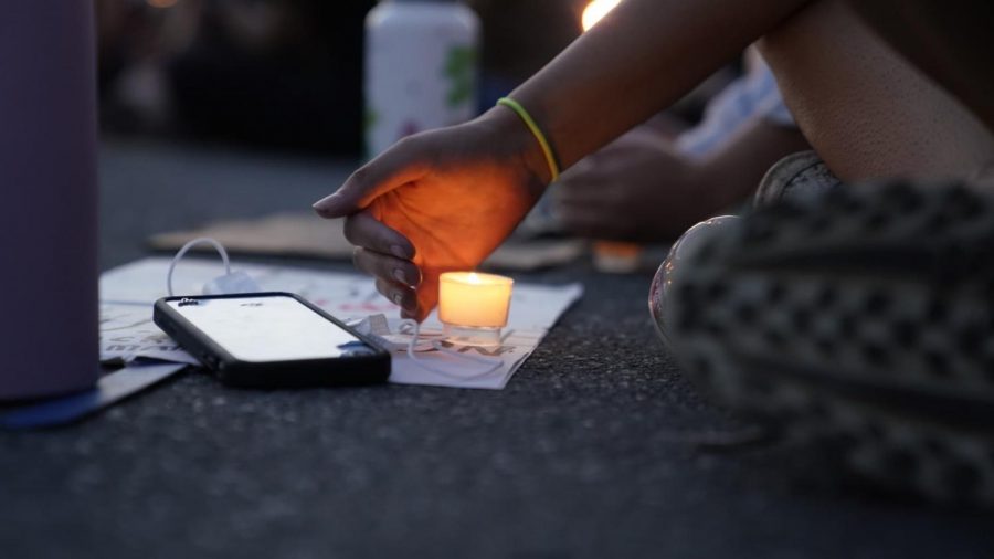 A protester sits by a candle to remember George Floyd.