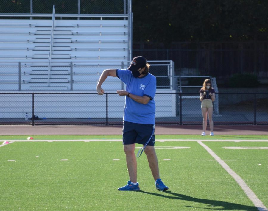 Varsity field hockey coach Mary Donahue demonstrates a stick skill to her practice cohort. With the transition to in-person practices during the COVID-19 pandemic, only 14 athletes per coach are allowed, masks must be worn when players are not engaging in strenuous activity and social distancing rules are required.