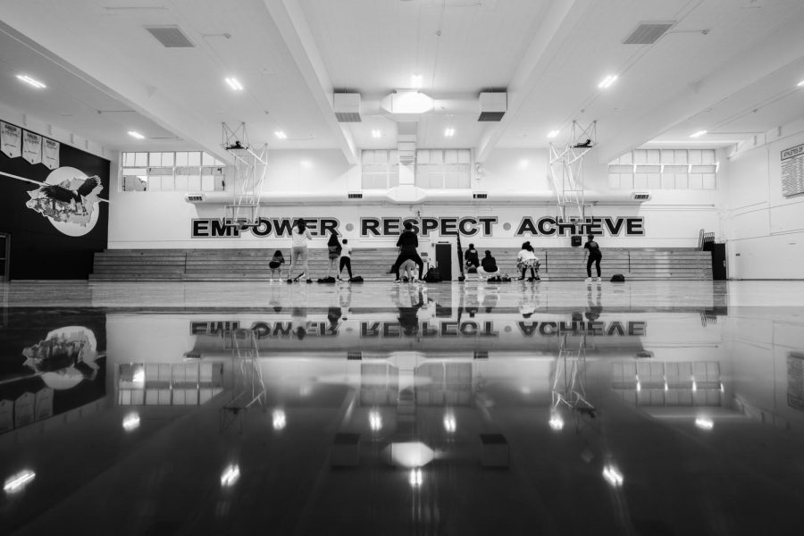 Students do air squats in order to complete a workout circuit in the school gym.