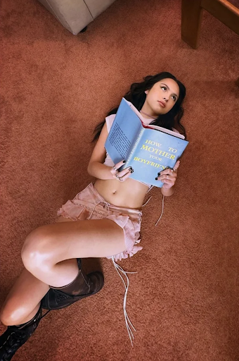 Singer-songwriter Olivia Rodrigo flips through a book titled “How to Mother Your Boyfriend” for the music video of her song, “get him back!”