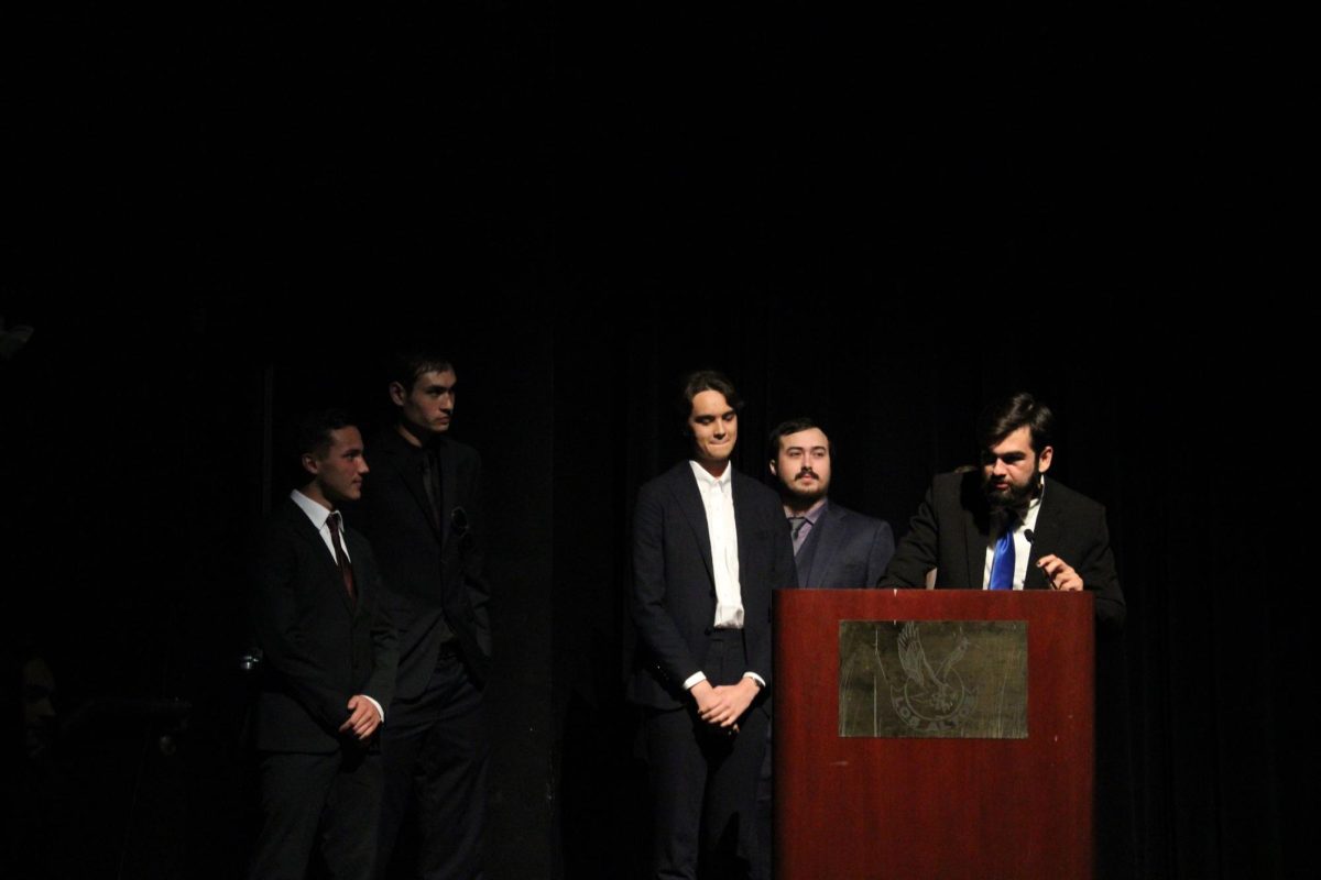 Filmmaking crew members of Passenger Princess stand at the microphone and podium while senior Razvan Popescu speaks.