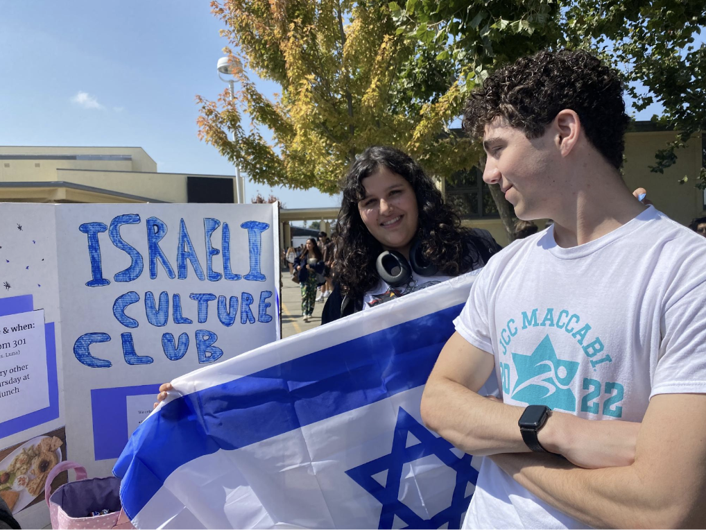 Junior Ariana Tsur holding the Israeli flag while junior Ori Gillai looks at their club sign. 