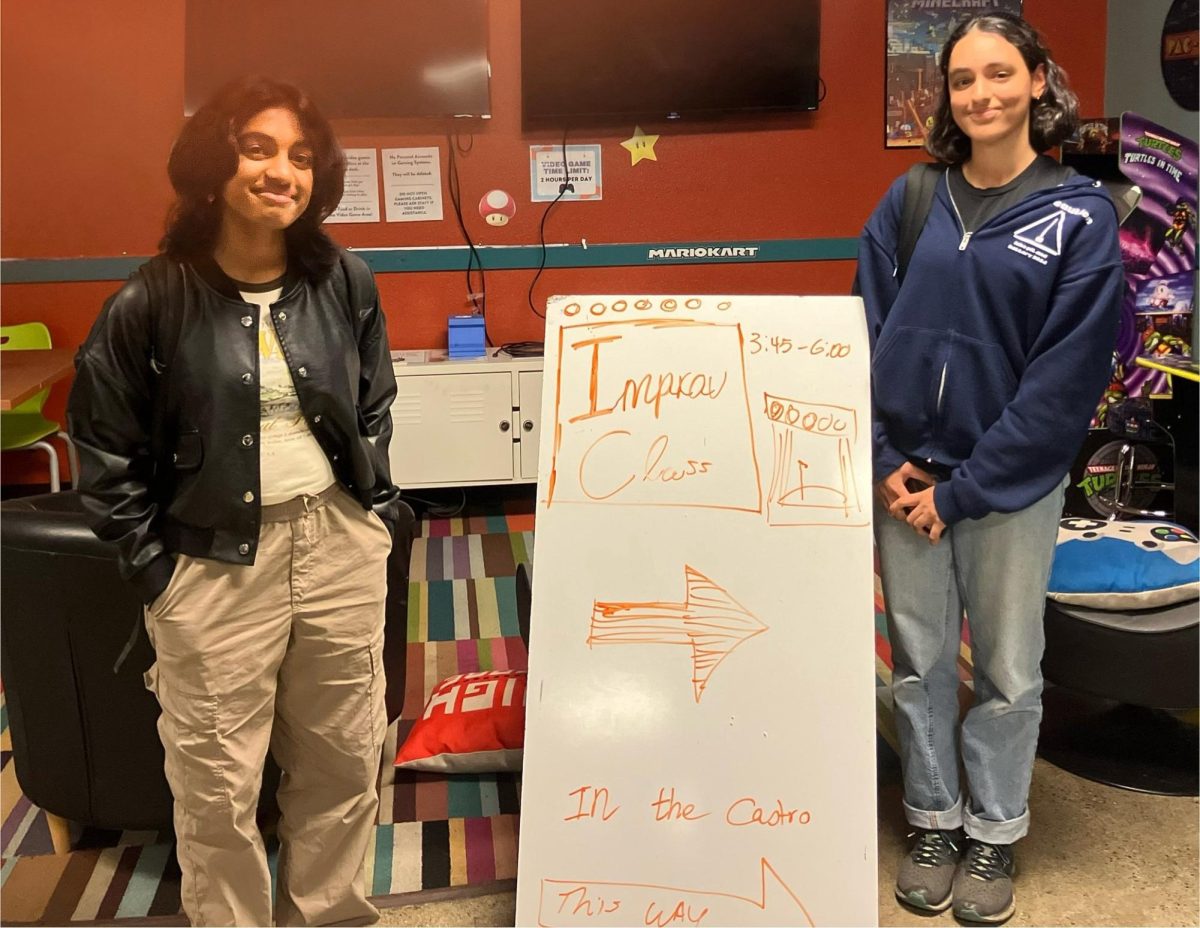 Avni and Jaya stand with an improv workshop sign at the Mountain View Teen Center. From 3:45 p.m. to 6:00 p.m., they introduced improvisational theater to a group of children.