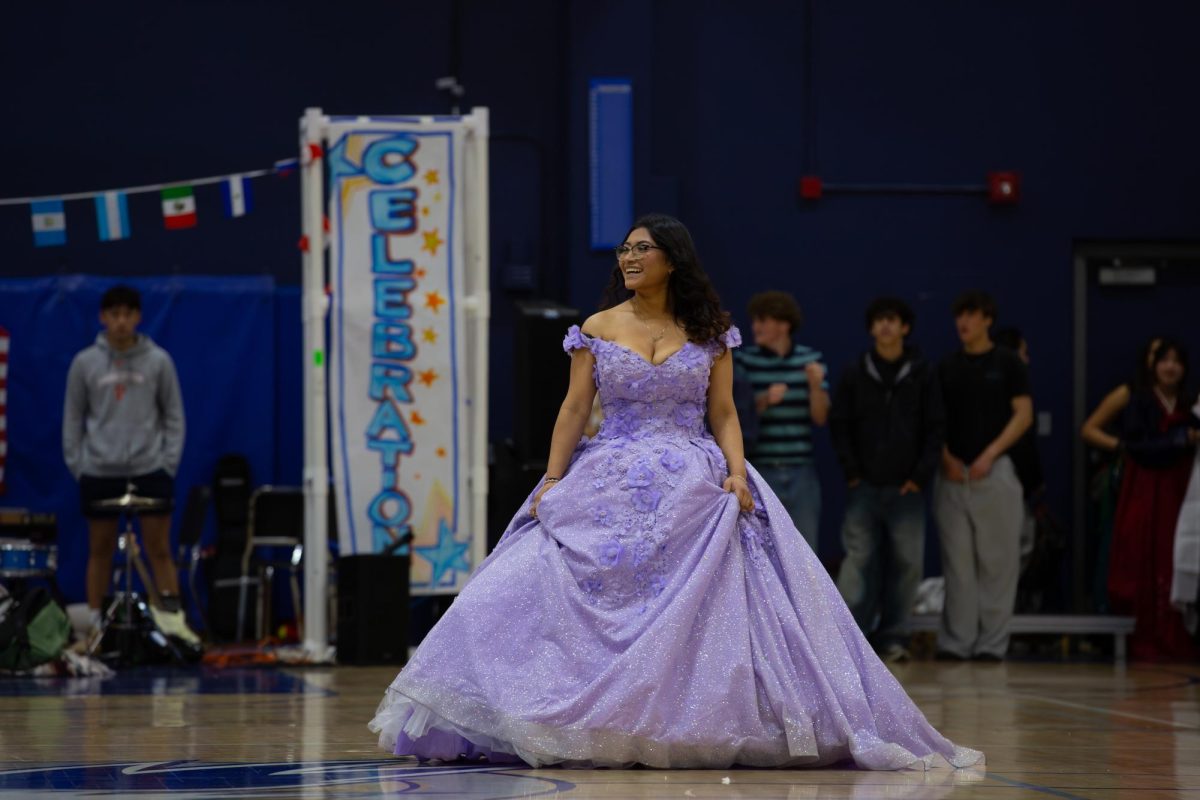 A student walks down the diversity rally runway wearing a purple quince dress. 