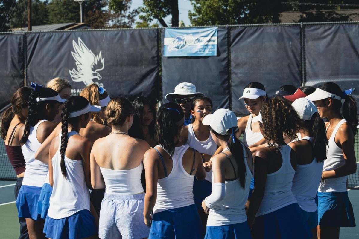The varsity girls tennis team huddles together and chants their team cheer before their first rivalry game. 