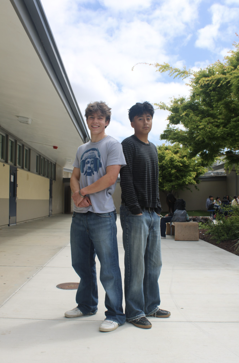 Left to right: Seniors Diego Castillas and Diogo Perez pose together in streetwear. Diego wears a graphic t-shirt, medium wash jeans and Gucci sneakers. Diogo wears a striped long sleeve, loose bootcut jeans, and adidas gazelles. 